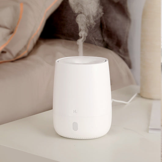 White minimalist aroma diffuser emitting mist, with a single button, on a white nightstand next to a bed. - Image 8