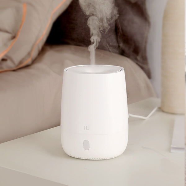 White minimalist aroma diffuser emitting mist, with a single button, on a white nightstand next to a bed. - Image 3