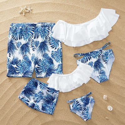 Family matching swimsuits with white and blue tropical leaf print, including men's shorts, women's and girl's ruffled one-shoulder bikinis. - Image 13