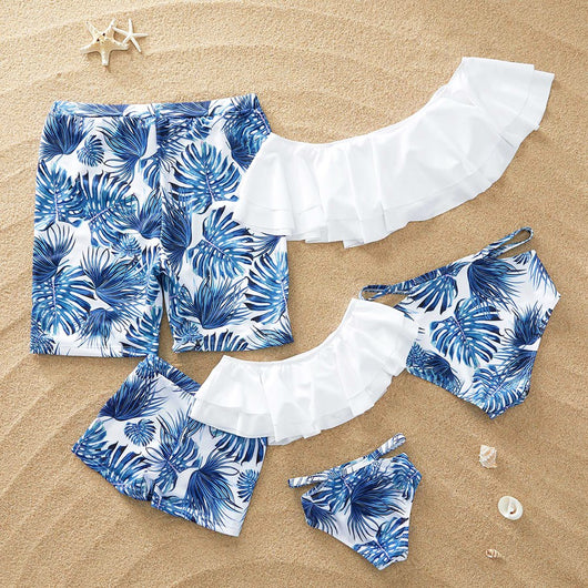 Family matching swimsuits with white and blue tropical leaf print, including men's shorts, women's and girl's ruffled one-shoulder bikinis. - Image 4