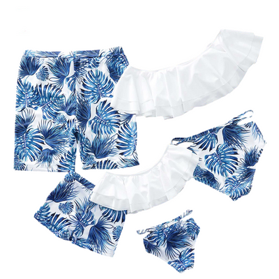 Family matching swimsuits with white and blue tropical leaf print, including men's shorts, women's and girl's ruffled one-shoulder bikinis. - Image 7