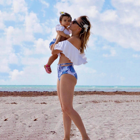 Family matching swimsuits with white and blue tropical leaf print, including men's shorts, women's and girl's ruffled one-shoulder bikinis. - Image 6