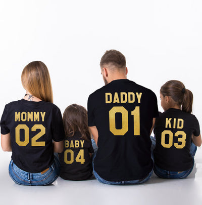 Family of four wearing matching black short-sleeved t-shirts with gold 'DADDY 01', 'MOMMY 02', 'KID 03', and 'BABY 04' text. - Image 3