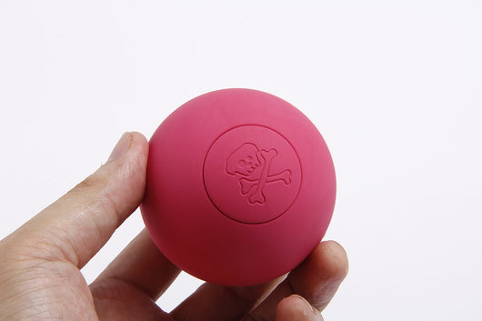Pink rubber pet bouncy ball with an embossed skull and crossbones design, held in a hand. - Image 6