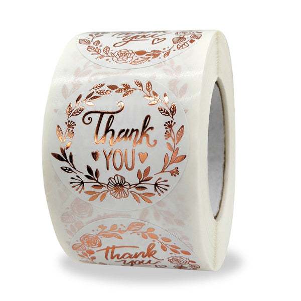 Roll of white paper 'Thank You' stickers with rose gold foil text and a delicate floral wreath design.