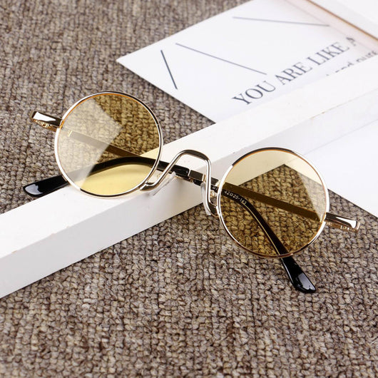 Retro round sunglasses with gold-colored frames and yellow tinted lenses, displayed on a textured surface.