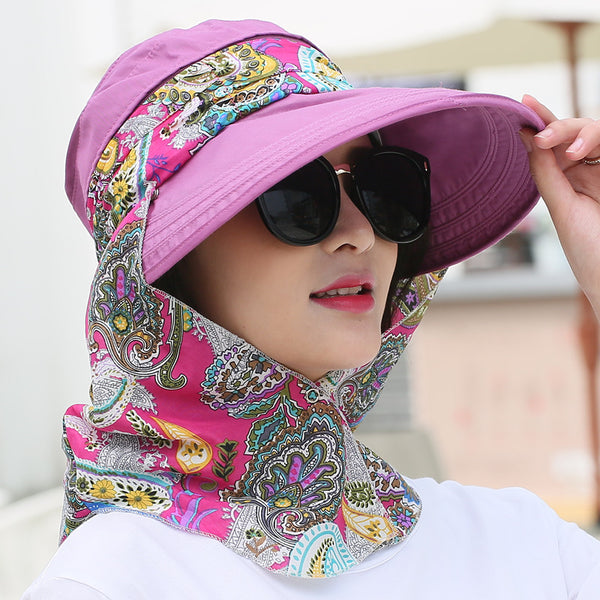 Woman wearing a light yellow wide-brim sun hat with a colorful paisley neck flap and dark sunglasses.