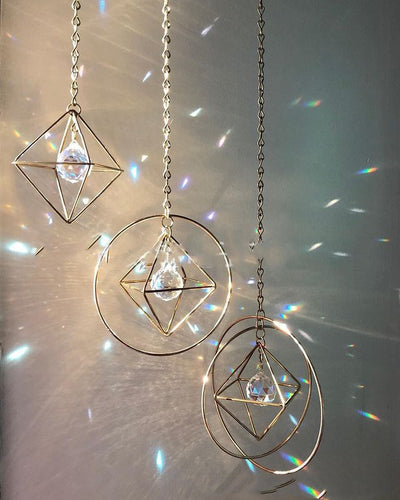Geometric iridescent suncatcher with a gold frame and dangling crystal pendants, held in a hand, creating rainbow light. - Image 6