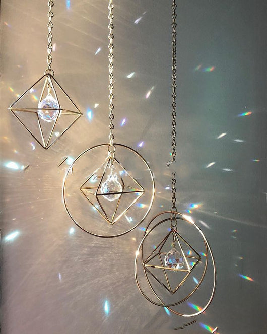 Geometric iridescent suncatcher with a gold frame and dangling crystal pendants, held in a hand, creating rainbow light. - Image 6