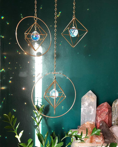 Geometric iridescent suncatcher with a gold frame and dangling crystal pendants, held in a hand, creating rainbow light. - Image 7