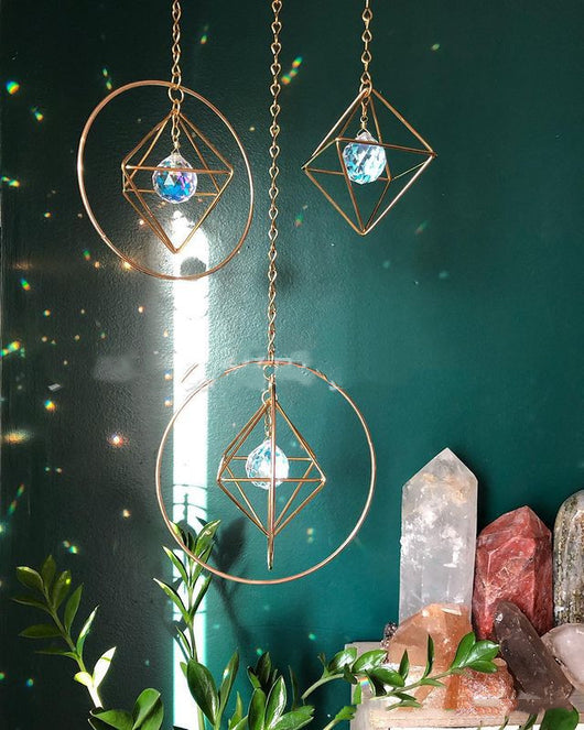 Geometric iridescent suncatcher with a gold frame and dangling crystal pendants, held in a hand, creating rainbow light. - Image 7