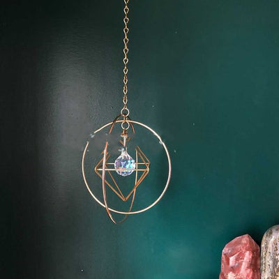 Geometric iridescent suncatcher with a gold frame and dangling crystal pendants, held in a hand, creating rainbow light. - Image 4