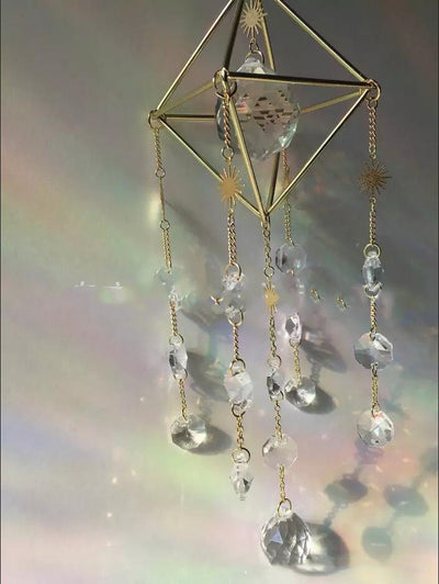 Geometric iridescent suncatcher with a gold frame and dangling crystal pendants, held in a hand, creating rainbow light. - Image 3