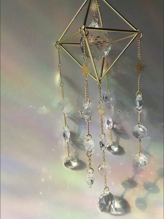 Geometric iridescent suncatcher with a gold frame and dangling crystal pendants, held in a hand, creating rainbow light. - Image 3