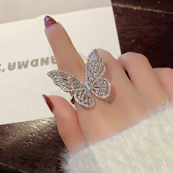 Sparkling silver-tone butterfly ring with clear baguette and round cut stones on a white surface.