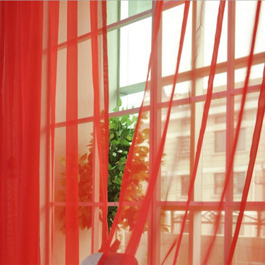 Close-up of a solid red sheer tulle curtain hanging in front of a window, allowing light to filter through.