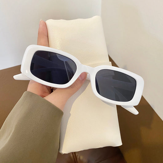 Black rectangular retro sunglasses with dark lenses held by a hand over a cream display pillow. - Image 6