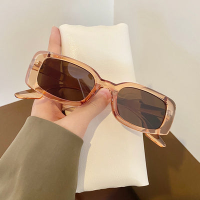 Black rectangular retro sunglasses with dark lenses held by a hand over a cream display pillow. - Image 7
