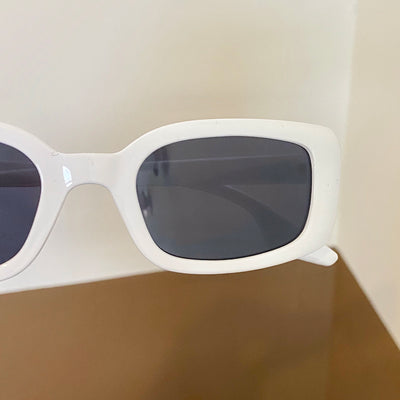Black rectangular retro sunglasses with dark lenses held by a hand over a cream display pillow. - Image 5