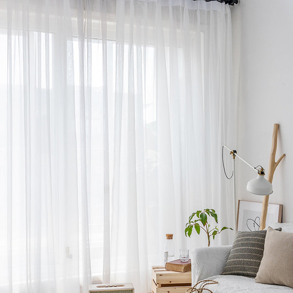 Light green sheer curtains hanging on a rod, one tied back, in a modern living room with white walls.