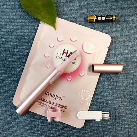 Pink electric shaver with cap off, showing blade, comb attachment, cleaning brush, and AA battery on a pink sheet mask. - Image 3