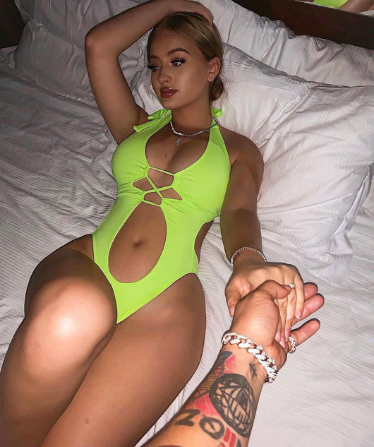 Woman wearing a black one-piece swimsuit with a halter neck, criss-cross front, and torso cut-outs, lying on a bed. - Image 7