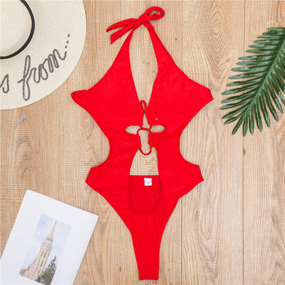 Woman wearing a black one-piece swimsuit with a halter neck, criss-cross front, and torso cut-outs, lying on a bed. - Image 11