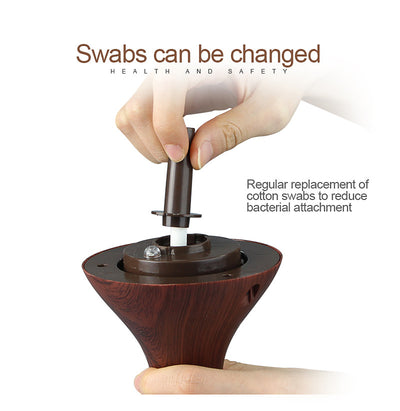 Dark wood grain LED essential oil diffuser with a blue light band and touch switch, shown with a hand operating it. Includes a bundle of 10 white filter sticks. - Image 15