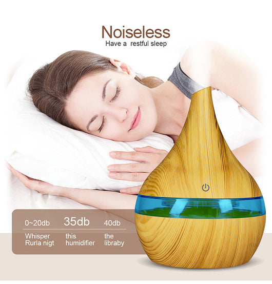 Dark wood grain LED essential oil diffuser with a blue light band and touch switch, shown with a hand operating it. Includes a bundle of 10 white filter sticks. - Image 16