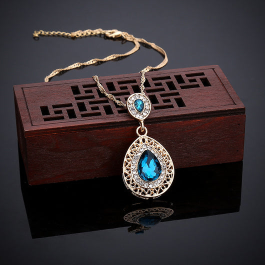 Gold-toned necklace and matching drop earrings set with blue teardrop crystals and clear rhinestones, on a wooden box. - Image 16