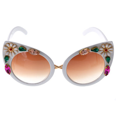 White cat-eye sunglasses with brown gradient lenses, adorned with clear and amber rhinestone flowers and bees.