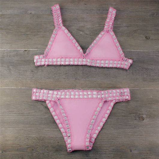 Pink crocheted bikini with silver knitted stitching, featuring a triangle top and matching bottom, laid flat.