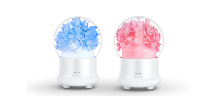 White aromatherapy machine with a clear dome top, featuring blue preserved flowers and an aqua glow. Includes 'LIGHT' and 'MIST' controls.
