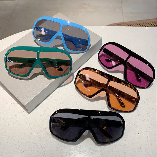Oversized women's shield sunglasses with a tortoiseshell frame and brown-tinted lenses, held by a hand.