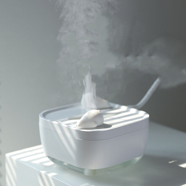 White ultrasonic humidifier with a clear base and a cute polar bear figurine on top, emitting a fine mist.