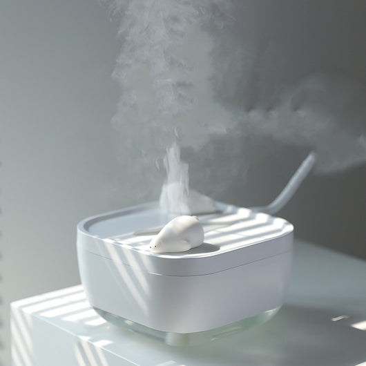 White ultrasonic humidifier with a clear base and a cute polar bear figurine on top, emitting a fine mist.