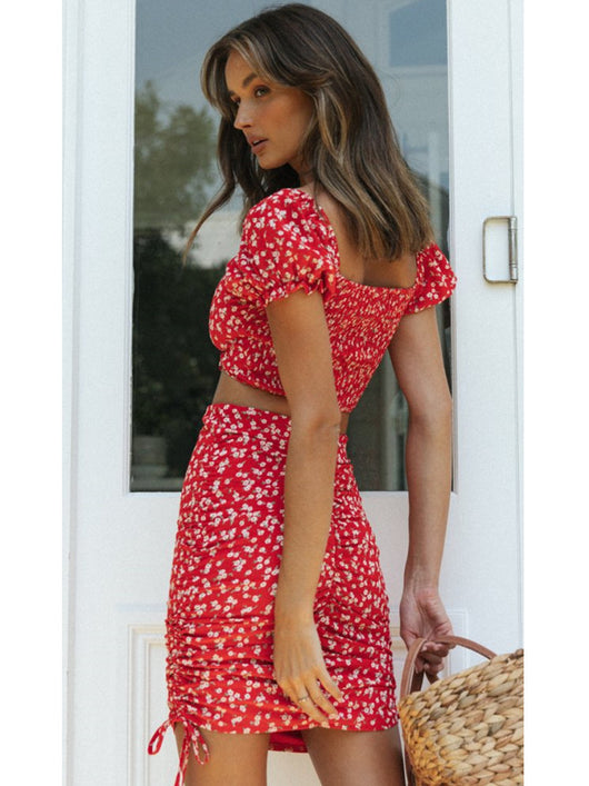 Smiling woman in a red floral print crop top and matching ruched mini skirt with side ties. - Image 4