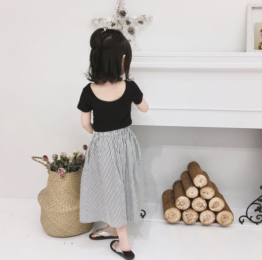 Young girl wearing a black short-sleeve crop top and a grey and white striped midi skirt with flip-flops. - Image 3
