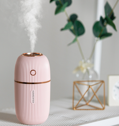 Pink mini ultrasonic air humidifier with ribbed texture and rose gold accents, emitting a fine mist on a white shelf. - Image 4