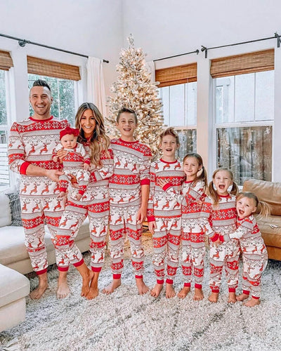 Family of seven wearing matching red and white Christmas pajamas with reindeer and snowflake patterns in a living room. - Image 19