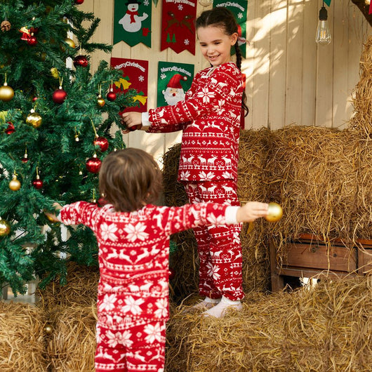 Family of four wearing matching red and white Christmas pajamas with reindeer and snowflake patterns, smiling. - Image 13
