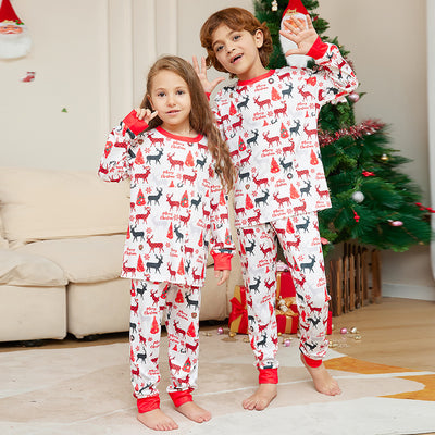 Young girl in white Christmas pajamas with red deer and tree print, red trim, standing by a decorated tree. - Image 9