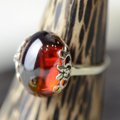 Silver ring with a large, round, deep red gemstone set in an ornate filigree bezel, displayed on a textured surface. - Image 5