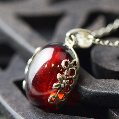 Silver ring with a large, round, deep red gemstone set in an ornate filigree bezel, displayed on a textured surface. - Image 3