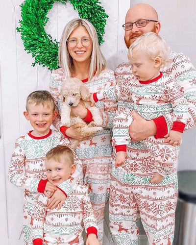 Family of four wearing matching green and white Christmas pajamas with fair isle print and red trim, sitting on a bed. - Image 11