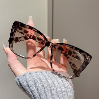 Clear large-frame square glasses held by a hand in a grey knitted sweater, showcasing the transparent plastic frame. - Image 11