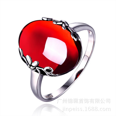 Silver ring with a large, round, deep red gemstone set in an ornate filigree bezel, displayed on a textured surface. - Image 2