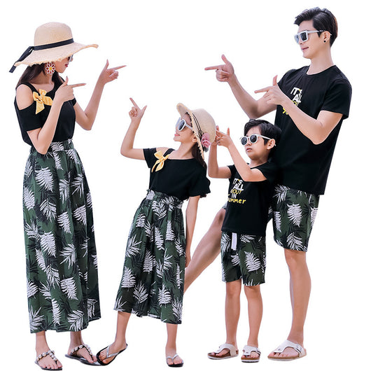 Family of four in matching black and green tropical print outfits on a beach, featuring t-shirts, shorts, skirt, and wide-leg pants. - Image 3
