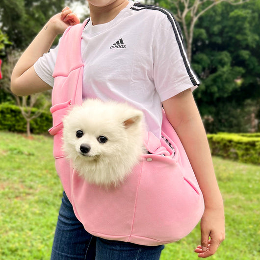Person in white hoodie carrying a happy white dog in a navy blue pet sling bag outdoors. - Image 10