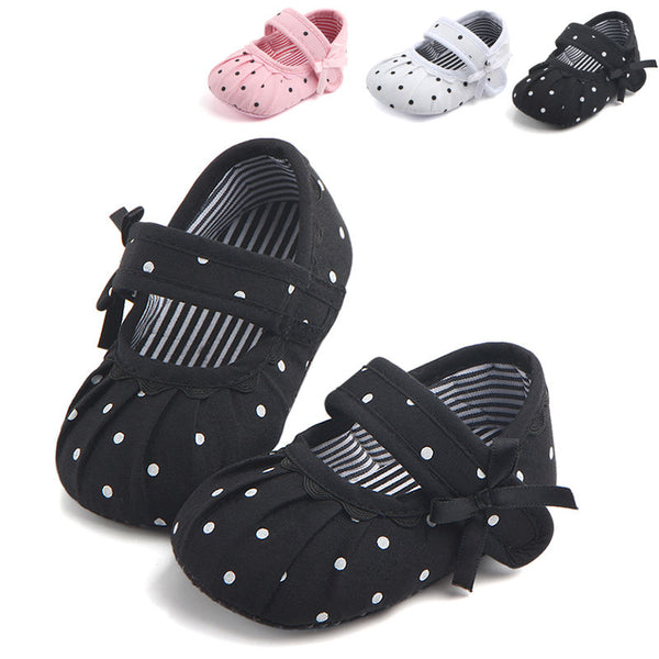 Black baby girl Mary Jane shoes with white polka dots, a strap, bow accent, and striped lining.